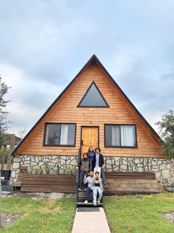 Familia posando en la escalera de madera de una cabaña alpina rústica bajo un cielo nublado